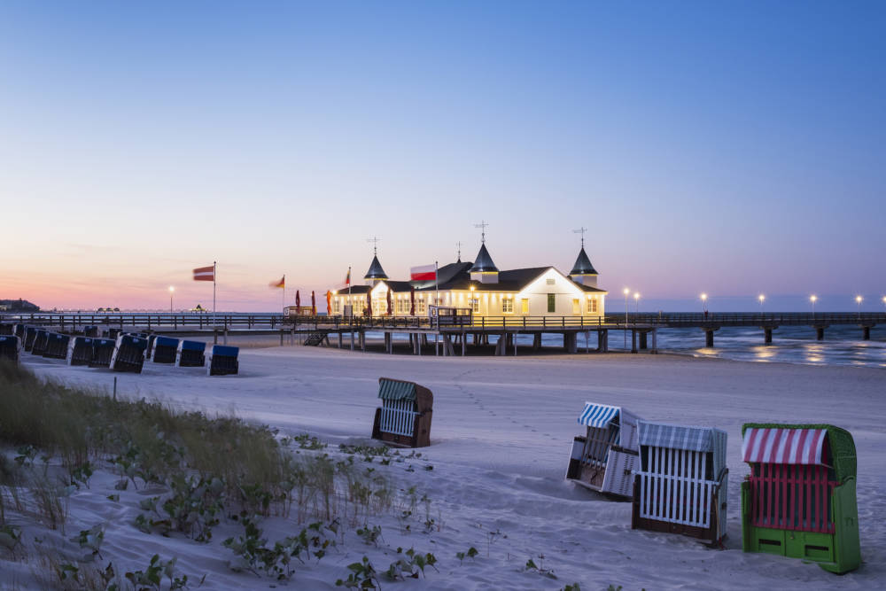 Germany, Usedom, Ahlbeck, view to lighted sea bridge with hooded beach chairs in the foreground at dusk