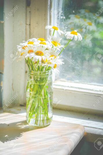 bouquet of daisies in glass jar near the window