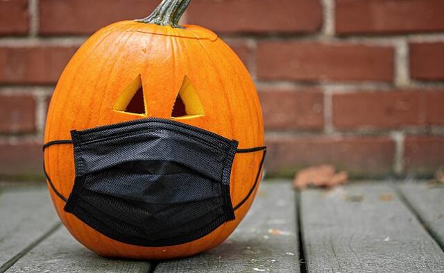 Carved pumpkin for Halloween wearing a Covid 19 face mask on a porch with a brick background