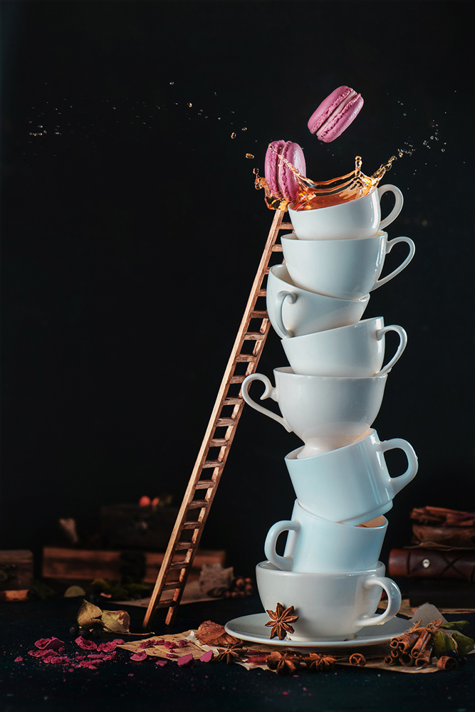 Tower of white coffee cups with a ladder, macaroons, splash and coffee drops on a dark background. Indulgence concept. Action food photography.