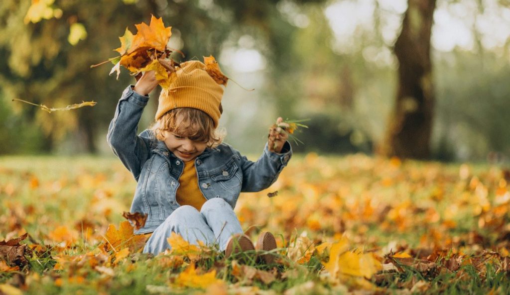 Kind spielt mit Blättern im Herbst