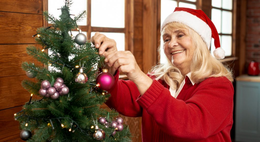 Seniorin schmückt allein den Weihnachtsbaum